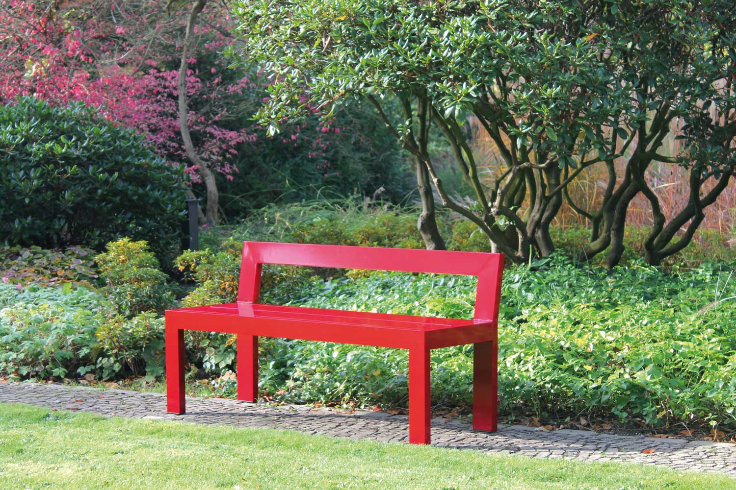 Rote Gartenbank - Farbenfrohe, leichte Solitärbank für den Garten, die immer zum Blickfang wird - Schöner sitzen. Als farbenfroher Akzent im Garten lädt diese Bank ein, neue Blickwinkel im Garten zu entdecken. Als Solitärbank schafft sie einen Ort zum Verweilen, wo man sonst nie sitzen würde, bietet aber auch einer bunten Gesellschaft spontan Sitzplatz, da sie leicht getragen werden kann. Ihre Schlichtheit in der Form erzeugt zudem einen spannenden Kontrast zur Flora im Garten und bringt auch versteckte Ecken im Garten zur Geltung.